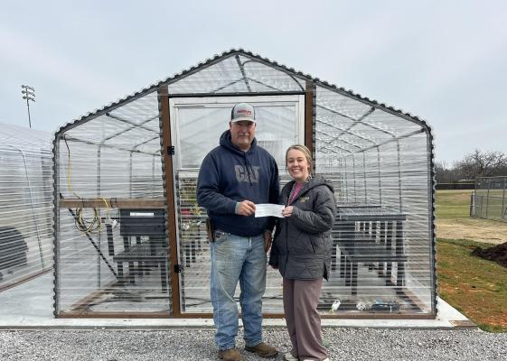 Madison County Farm Bureau Board President Kevin Counsil (left) presents a check to North Zulch FFA teacher Heather Wieghat in front of the new greenhouse at North Zulch High School. PHOTO COURTESY OF MADISON COUNTY FARM BUREAU