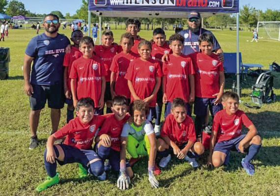 The Mustangs Blue team poses for a photo under their club tent at a recent tournament. Players sport their red jerseys with pride as they stand alongside their coaches. COURTESY PHOTO