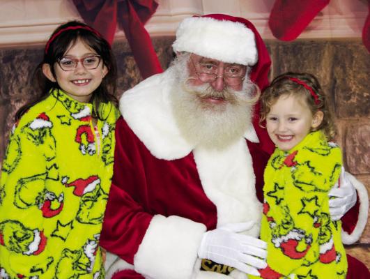 Two sisters in matching Grinch pajamas pose with Santa Claus at the Hispanic Heritage Association's second annual Christmas Toy Giveaway on Tuesday, Dec. 16 at the Lake Madison Front Pavilion. METEOR PHOTO BY RICHARD SIRMAN