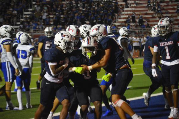 Phillip Green Jr. rises triumphant, mobbed by jubilant teammates after scoring the game-winning touchdown in overtime against Navasota Friday night at Mustang Stadium. Green's 10-yard rush sealed Madisonville's 27-20 victory. METEOR PHOTOS BY RICHARD SIRMAN 