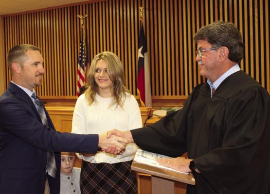 Aaron Campbell shakes hands with Madison County Judge Clark Osborne after taking his oath of office as Precinct 1 Constable. His wife, Abbie Campbell, watches proudly, &amp; their son pees through from behind during the swearing-in ceremony.