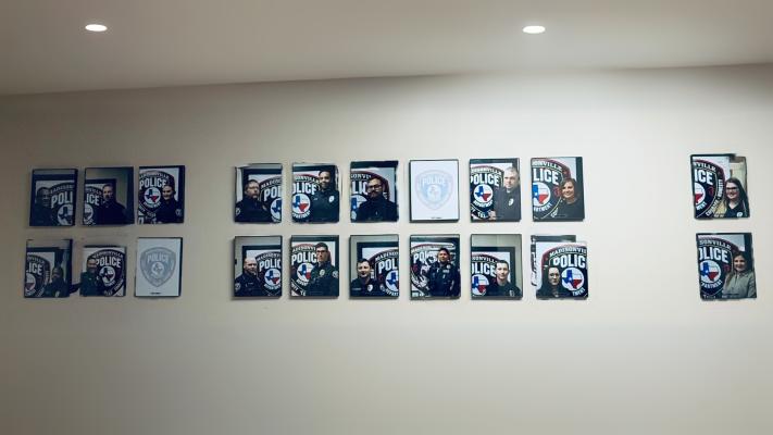 The Madisonville Police Department’s staff wall displays framed portraits of officers and department personnel. Chief Herbert Gilbert points to this display as one of the “minor things” that has boosted morale, transforming a previously bare wall into a visual representation of the department’s growth from five officers in 2024 to a fully staffed force of 19 employees. METEOR PHOTO BY RICHARD SIRMAN
