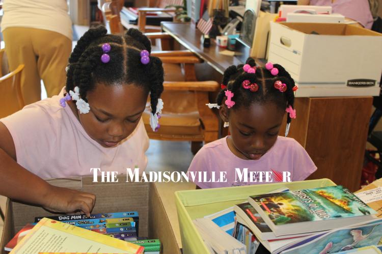 METEOR PHOTO BY RICHARD SIRMAN Autumn and Aubrey Ford, granddaughters of Midway Alderwoman Brenda Ford, search through boxes of donated books Friday at City Hall. The city’s free summer reading program launched May 29 and sends children home with a new book of their own every Friday, running through Aug. 7.